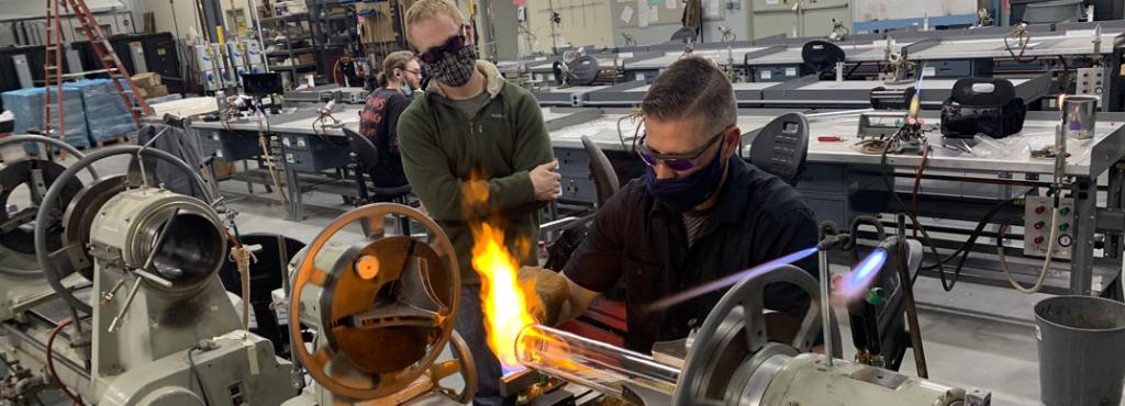 Teacher demonstrating on a lathe for a student inside the Glass Education Center 