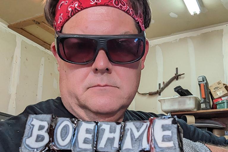 Artist Stephen Boehme holding up flameworked letters creating his name, BOEHME