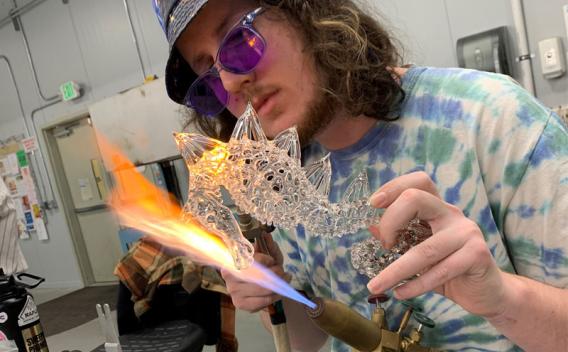Student creating a glass seahorse sculpture on a torch