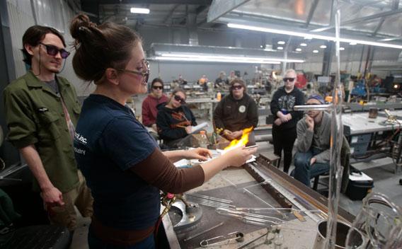 Instructor in the glass center teaching student the flameworking process of glassmaking 