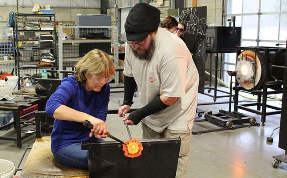 Man instructing a woman creating a glass object in the glassblowing studio