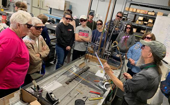 Group of people watching a man work with glass at a torch